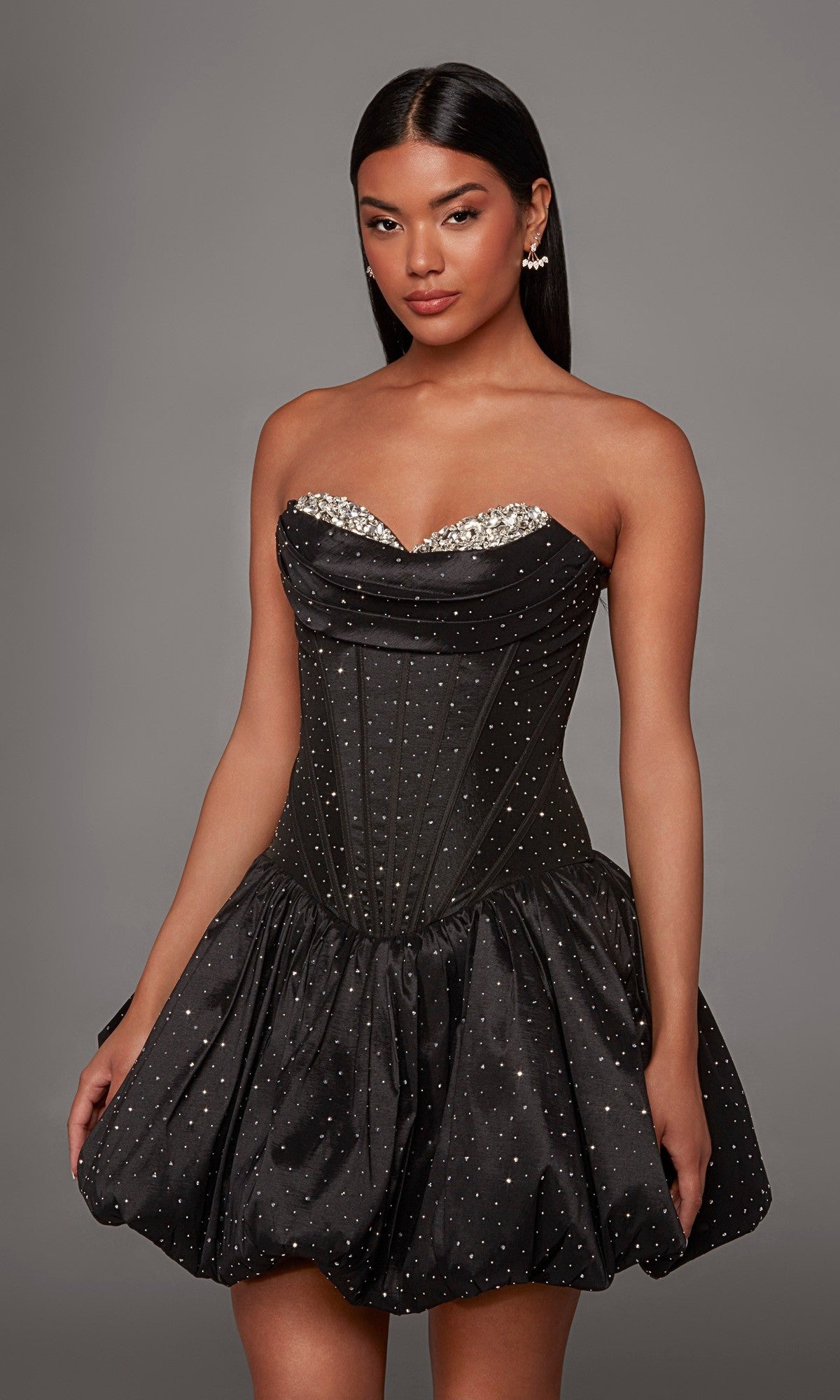 A woman poses against a plain gray background wearing the Short Homecoming Dress: Alyce 30125 in Black/Silver, featuring a strapless, rhinestone-embellished corset-style bodice and a bubble hem A-line skirt.
